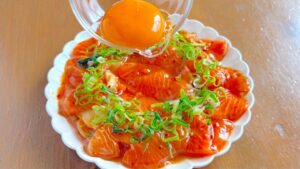 盛り付けたサーモンとキムチに卵黄をのせるところ