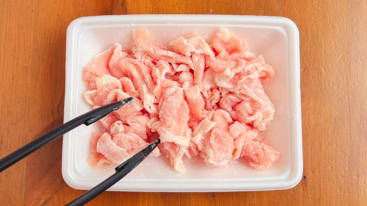 トレーの上で豚こま切れ肉に薄力粉をまぶした様子