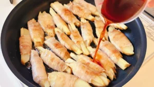 焼いた肉巻きへ照り焼きだれを加える様子
