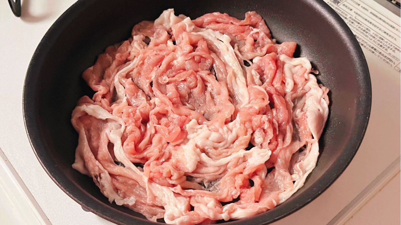 フライパンに豚こま切れ肉を敷き詰めた様子
