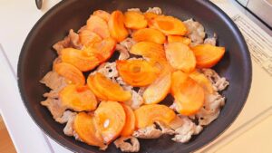 豚肉へ薄切りの柿を加えて炒める様子