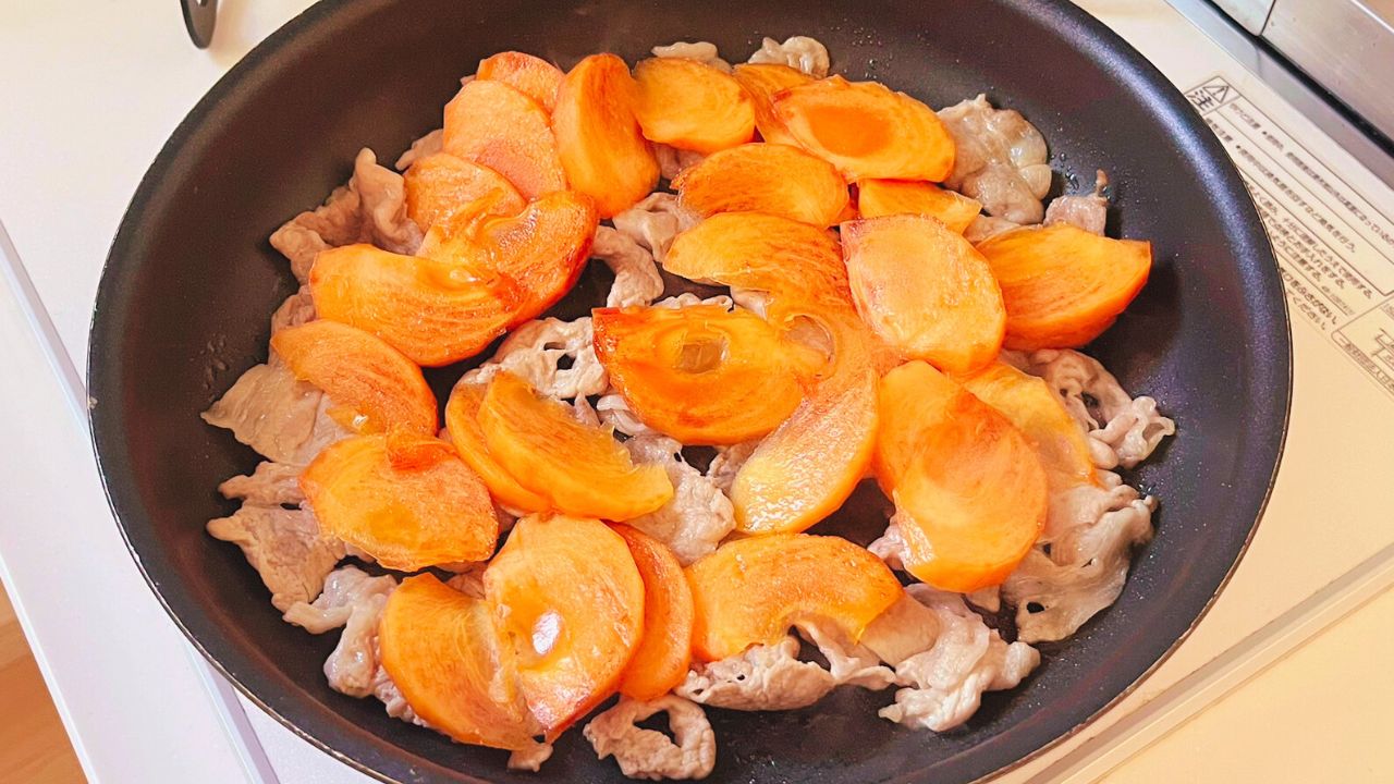 豚肉へ薄切りの柿を加えて炒める様子