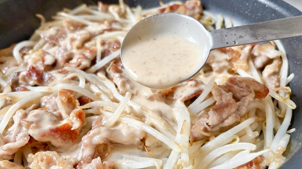 豚こま肉ともやしにごまドレッシングを加えている様子