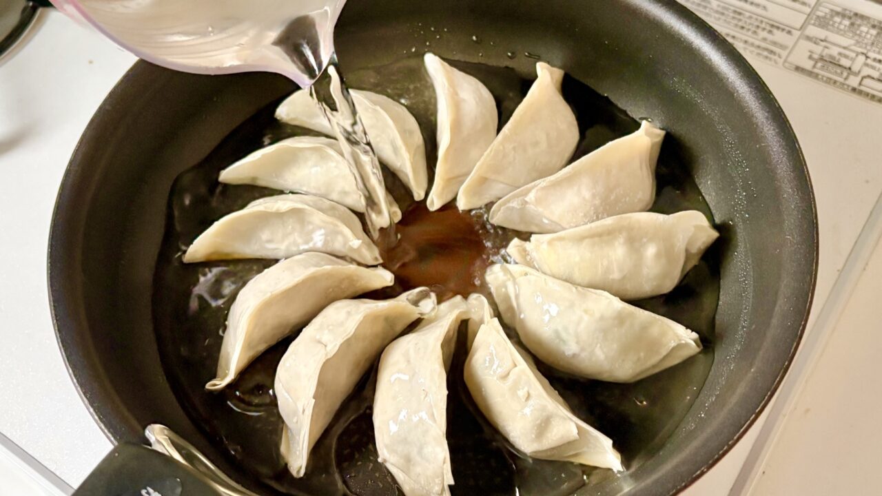 餃子を並べたフライパンに水を注ぐところ
